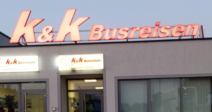 Gebäude mit Leuchtreklame K&K Busreisen über dem Eingang, fotografiert am Abend.