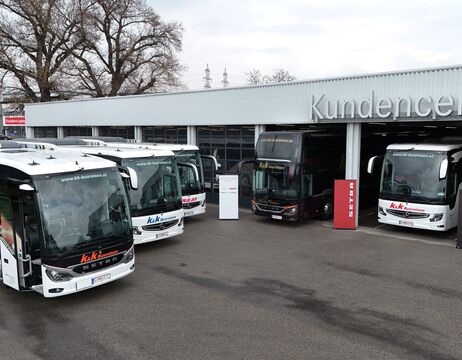 An einem bewölkten Tag sind mehrere große Busse vor einem Gebäude mit der Aufschrift Kundencenter geparkt.