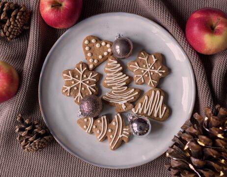 Ein Teller mit dekorierten Weihnachtsplätzchen mit Ornamenten, Äpfeln und Tannenzapfen auf einem strukturierten Tuch.
