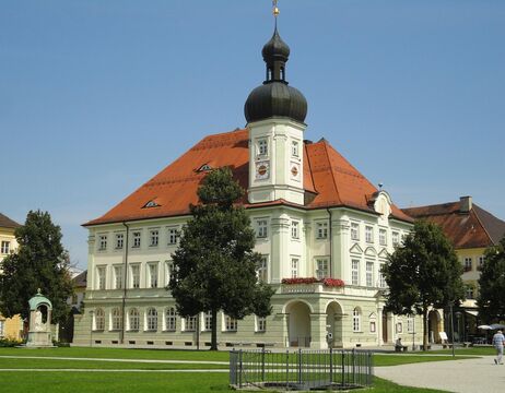 Ein historisches Gebäude mit einem roten Dach, weißen Wänden und einer hohen Zwiebelkuppel, umgeben von Bäumen und Gras.