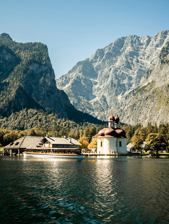 Eine Kirche am See mit roten Kuppeln und Bergen im Hintergrund an einem klaren, sonnigen Tag.