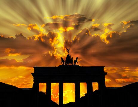 Silhouette des Brandenburger Tors bei Sonnenuntergang mit dramatischen Sonnenstrahlen, die durch die Wolken brechen.