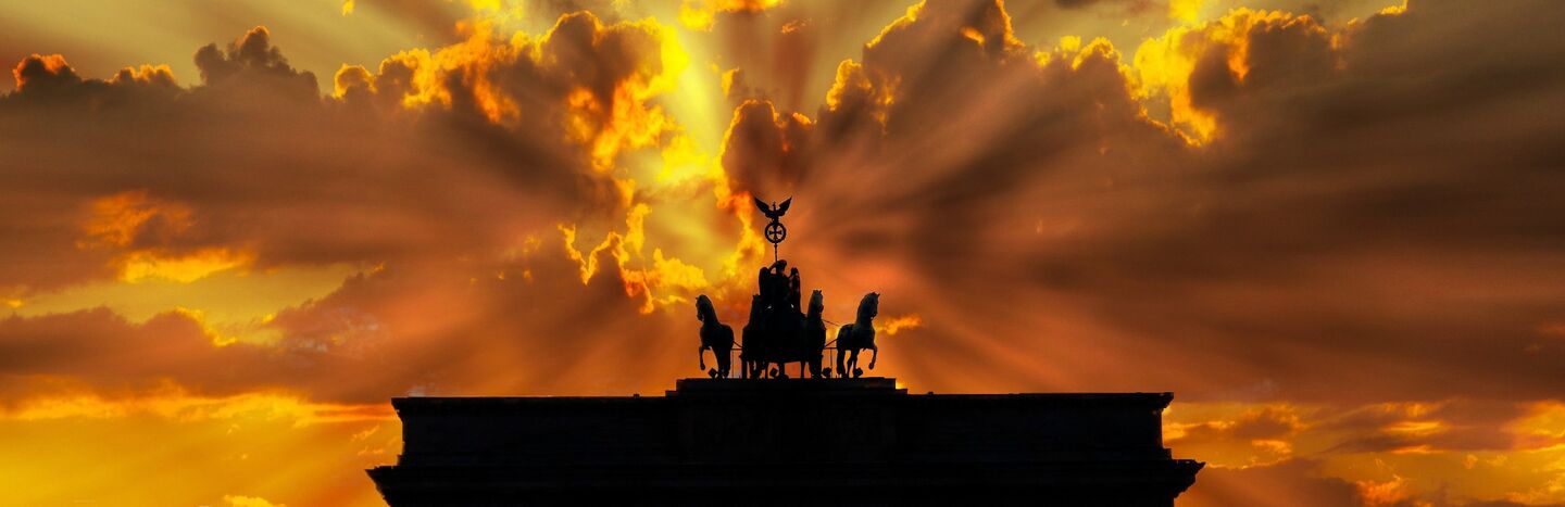 Silhouette des Brandenburger Tors bei Sonnenuntergang mit dramatischen Sonnenstrahlen, die durch die Wolken brechen.