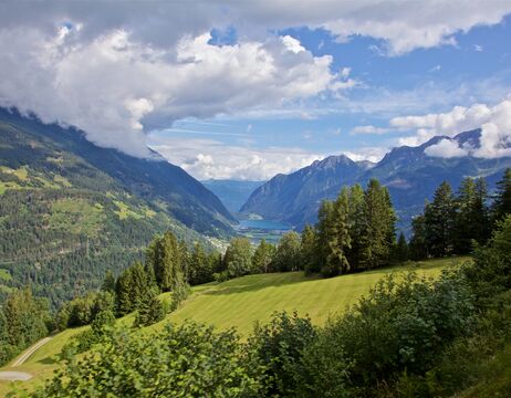 Grünes Tal mit Bäumen und Bergen unter einem blauen Himmel mit Wolken.