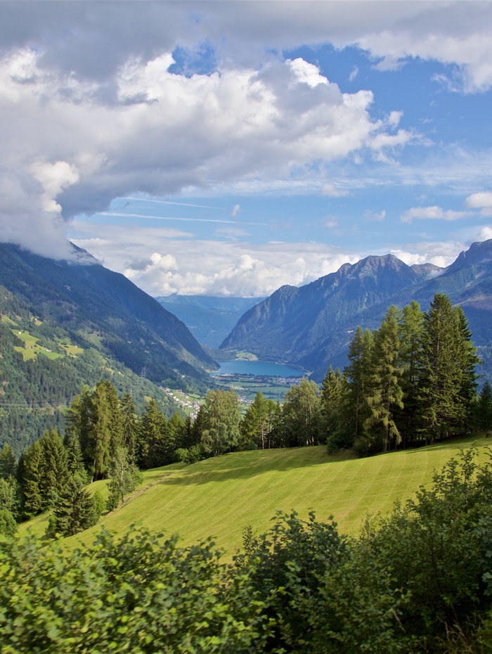 Grünes Tal mit Bäumen und Bergen unter einem blauen Himmel mit Wolken.