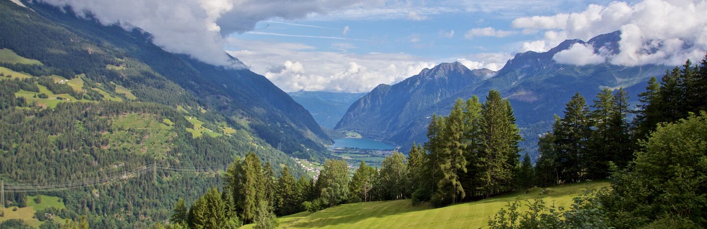 Grünes Tal mit Bäumen und Bergen unter einem blauen Himmel mit Wolken.