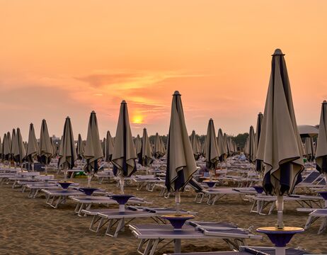 Geschlossene Sonnenschirme und leere Liegestühle am Sandstrand bei Sonnenuntergang.
