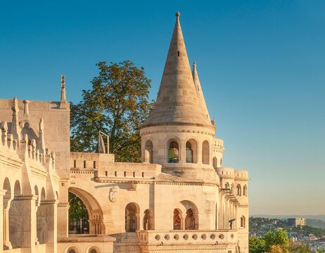 Steintürme und Treppen der Fischerbastei in Budapest, Ungarn, mit warmem Sonnenlicht und grüner Umgebung.