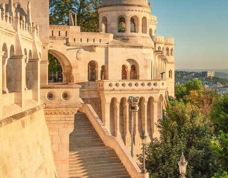 Steintürme und Treppen der Fischerbastei in Budapest, Ungarn, mit warmem Sonnenlicht und grüner Umgebung.