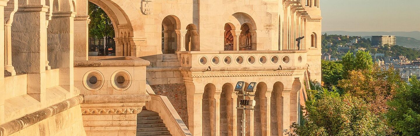 Steintürme und Treppen der Fischerbastei in Budapest, Ungarn, mit warmem Sonnenlicht und grüner Umgebung.