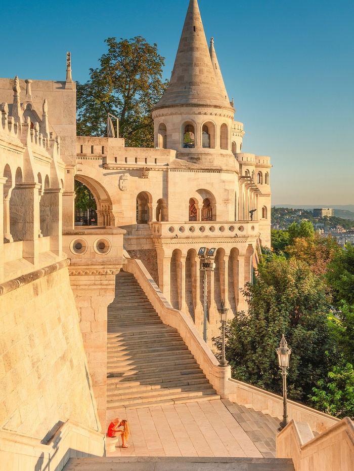 Steintürme und Treppen der Fischerbastei in Budapest, Ungarn, mit warmem Sonnenlicht und grüner Umgebung.