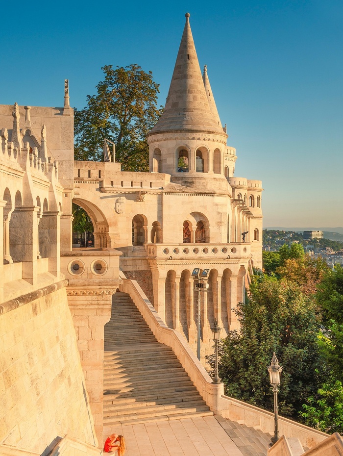 Steintürme und Treppen der Fischerbastei in Budapest, Ungarn, mit warmem Sonnenlicht und grüner Umgebung.