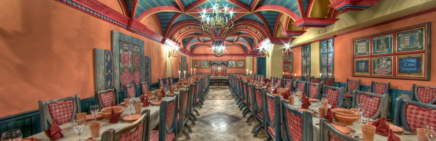 Langer Speisesaal mit farbenfroher Gewölbedecke, roten Stühlen, gedeckten Tischen und verzierten Kronleuchtern.