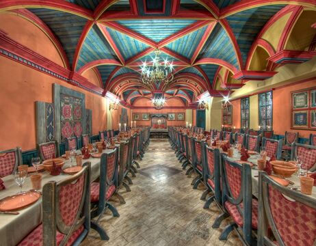 Langer Speisesaal mit farbenfroher Gewölbedecke, roten Stühlen, gedeckten Tischen und verzierten Kronleuchtern.