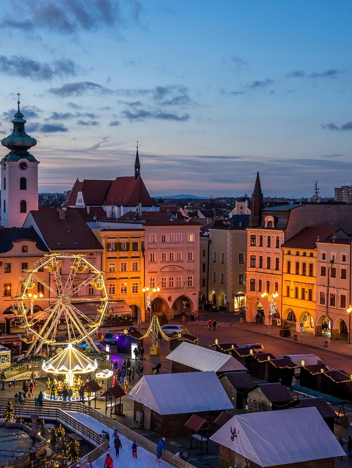 Stadtplatz in der Abenddämmerung mit Riesenrad, festlicher Beleuchtung und historischen Gebäuden im Hintergrund.
