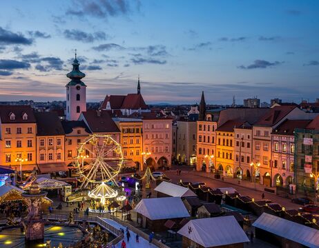 Stadtplatz in der Abenddämmerung mit Riesenrad, festlicher Beleuchtung und historischen Gebäuden im Hintergrund.