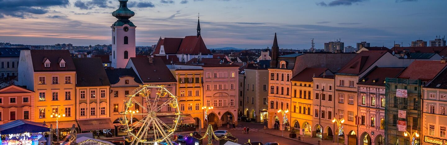 Stadtplatz in der Abenddämmerung mit Riesenrad, festlicher Beleuchtung und historischen Gebäuden im Hintergrund.