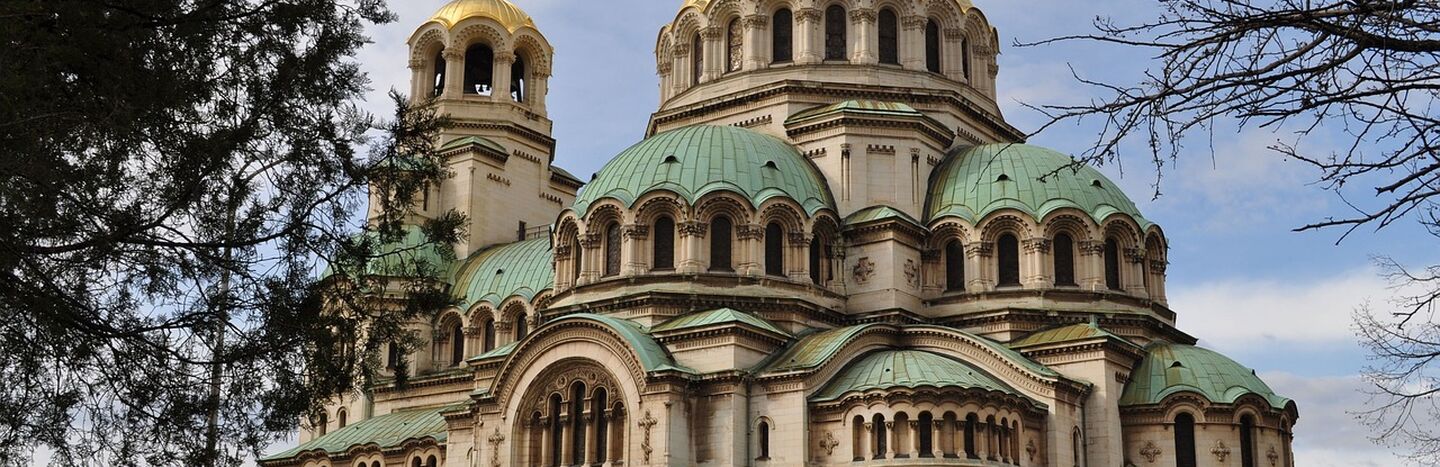 Orthodoxe Kathedrale mit grünen und goldenen Kuppeln, gewölbten Fenstern und detaillierter Steinarchitektur unter blauem Himmel.