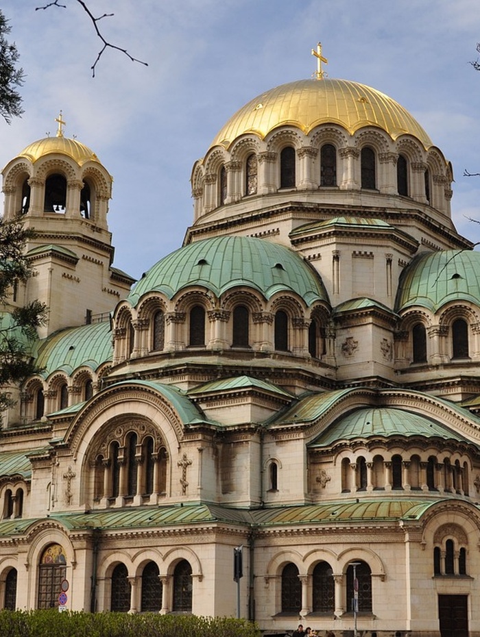 Orthodoxe Kathedrale mit grünen und goldenen Kuppeln, gewölbten Fenstern und detaillierter Steinarchitektur unter blauem Himmel.