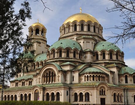 Orthodoxe Kathedrale mit grünen und goldenen Kuppeln, gewölbten Fenstern und detaillierter Steinarchitektur unter blauem Himmel.