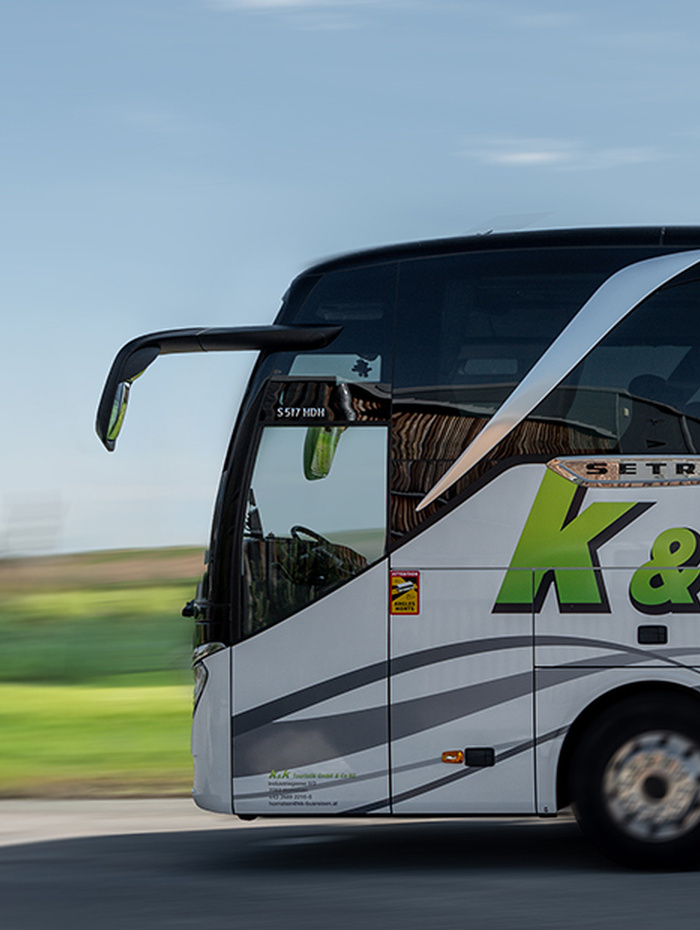 Ein weißer und grüner Reisebus fährt schnell auf einer Straße mit verschwommener Landschaft im Hintergrund.