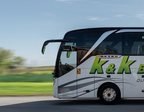 Ein weißer und grüner Reisebus fährt schnell auf einer Straße mit verschwommener Landschaft im Hintergrund.