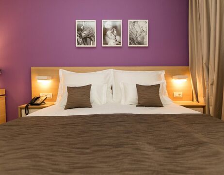 Ein ordentlich gemachtes Bett mit braunem und weißem Bettzeug, zwei Kissen und drei Schwarz-Weiß-Fotos darüber.