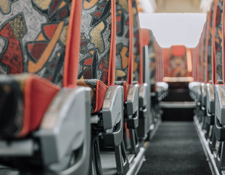 Reihen gemusterter, farbenfroher Sitze im Inneren eines Busses, vom Gang aus gesehen.