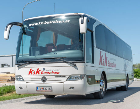 Weißer k&k Busreisen-Reisebus, geparkt auf einer Straße unter blauem Himmel.