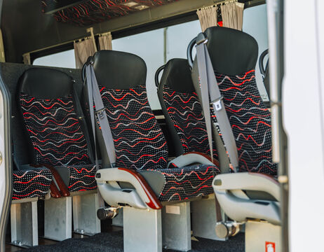 Vier Bussitze mit schwarz-rot gemusterten Polstern und Sicherheitsgurten in einem Fahrzeug.