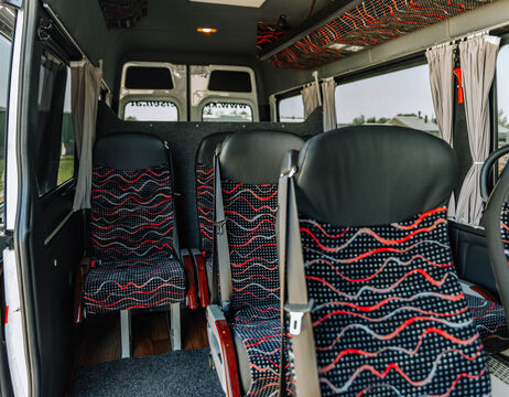 Reihen von gemusterten Bussitzen in einem Minibus mit Fenstern und Vorhängen auf beiden Seiten.