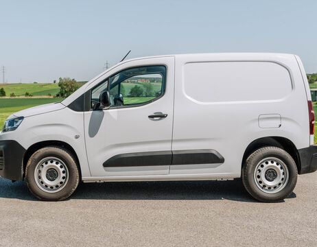 Weißer Lastwagen, der auf einer Straße mit grünen Feldern und einem klaren Himmel im Hintergrund geparkt ist.