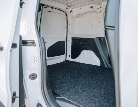Offener Laderaum eines weißen Lieferwagens mit dunklem Teppichboden und ohne Sitze oder Ladung im Inneren.