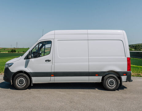 Weißer Transporter, geparkt auf einer Straße mit grünen Feldern und blauem Himmel im Hintergrund.