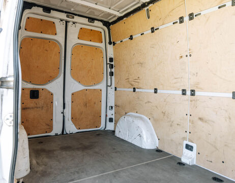 Innenraum eines leeren Transporters mit Holzverkleidung an den Wänden und geschlossenen hinteren Doppeltüren.