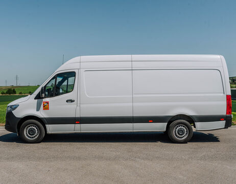 Ein weißer Transporter, der auf einer gepflasterten Straße mit Gras und blauem Himmel im Hintergrund geparkt ist.