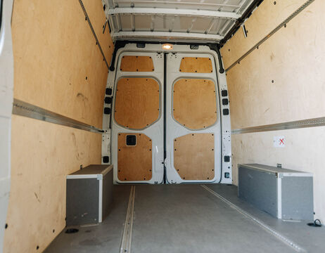 Innenansicht eines leeren Lieferwagens mit Holzverkleidung und zwei Staukästen in der Nähe der hinteren Türen.