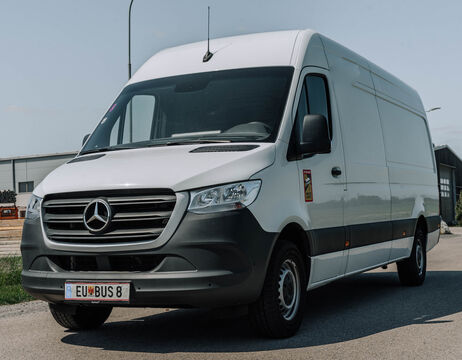 Ein weißer Mercedes-Benz-Lieferwagen ist auf einer asphaltierten Straße in der Nähe von Industriegebäuden geparkt.