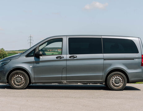 Ein grauer Lieferwagen parkt auf einer asphaltierten Straße mit Feldern und einer Stromleitung im Hintergrund.