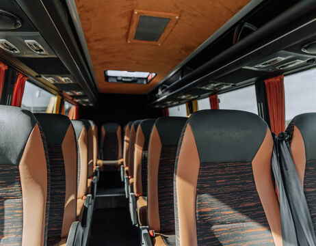 Leeres Interieur eines Reisebusses mit braunen und schwarzen Sitzen, roten Vorhängen und Ablagefächern im Dach.