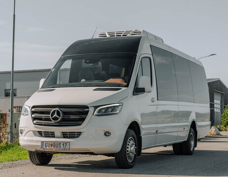 Ein weißer Mercedes-Benz Transporter mit einem Kühlaggregat ist auf einer Straße in der Nähe von Industriegebäuden geparkt.