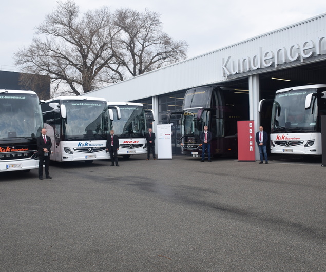 Fünf Personen stehen an einem bewölkten Tag neben vier großen Bussen vor einem Gebäude mit der Aufschrift Kundencenter.