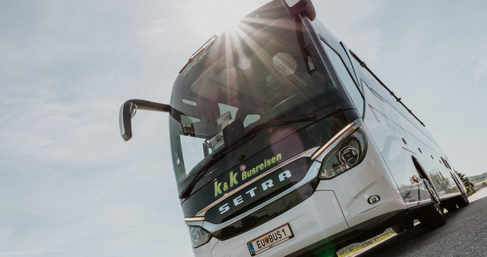 Weißer Setra-Reisebus, der im Sonnenlicht geparkt ist und auf dessen Vorderseite K&K Busreisen abgebildet ist.