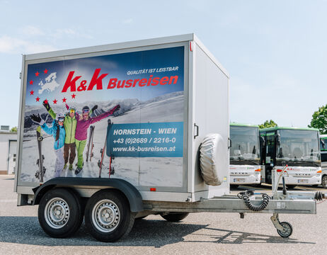 Ein K&K Busreisen-Anhänger zeigt auf der Seite eine Skireise-Werbung mit Menschen in Winterausrüstung.