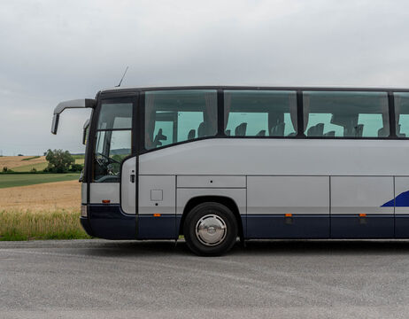 Seitenansicht eines geparkten Reisebusses auf einer Landstraße mit Feldern im Hintergrund.
