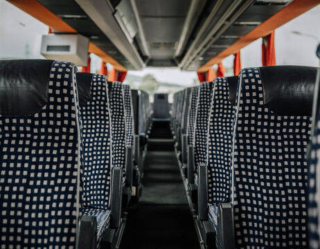 Blick auf leere gemusterte Sitze im Inneren eines modernen Busses, Blick durch den Gang auf die Frontscheibe.