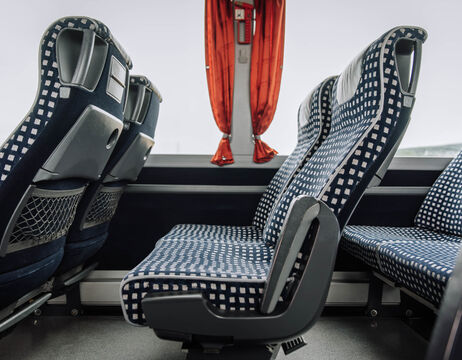 Blau-weiß gemusterte Bussitze neben einem Fenster mit roten Vorhängen, die an den Seiten zugezogen sind.