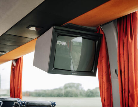 Alter Fernseher in einem Bus mit roten Vorhängen, die das Innere des Busses und die Sicht aus dem Fenster widerspiegeln.