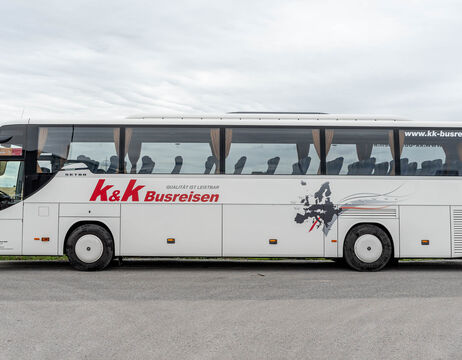 Weißer Reisebus mit dem Logo von K&K Busreisen und einer Landkartengrafik an der Seite, geparkt an einer Straße.