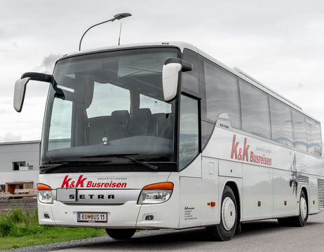 Weißer Setra Reisebus mit k&k Busreisen Schriftzug, geparkt auf einer Straße unter bewölktem Himmel.